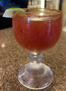 Chilled michelada cocktail with a spicy rim, garnished with a lime wedge in a goblet glass, a popular Mexican drink available at El Palmar Mexican restaurant in Carmichael, CA