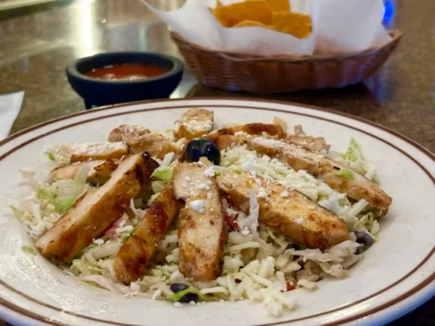 Grilled chicken breast strips Mexican Salad sprinkled with shredded cheese and garnished with a black olive, served with a side of salsa and a basket of tortilla chips, in a casual dining atmosphere at El Palmar Mexican restaurant in Carmichael, CA