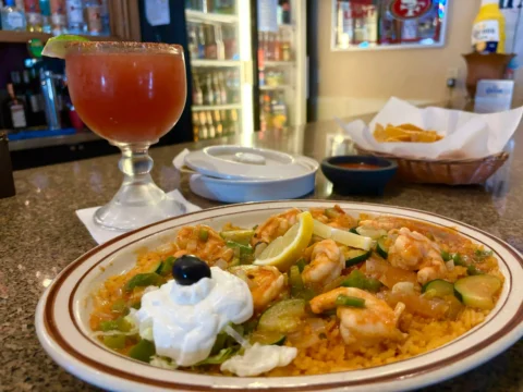 Sizzling shrimp fajitas with zucchini, green bell peppers, and onions over a bed of Mexican rice, garnished with a dollop of sour cream and a slice of lemon, accompanied by a side of salsa and warm tortillas, served at El Palmar Mexican restaurant in Carmichael, CA